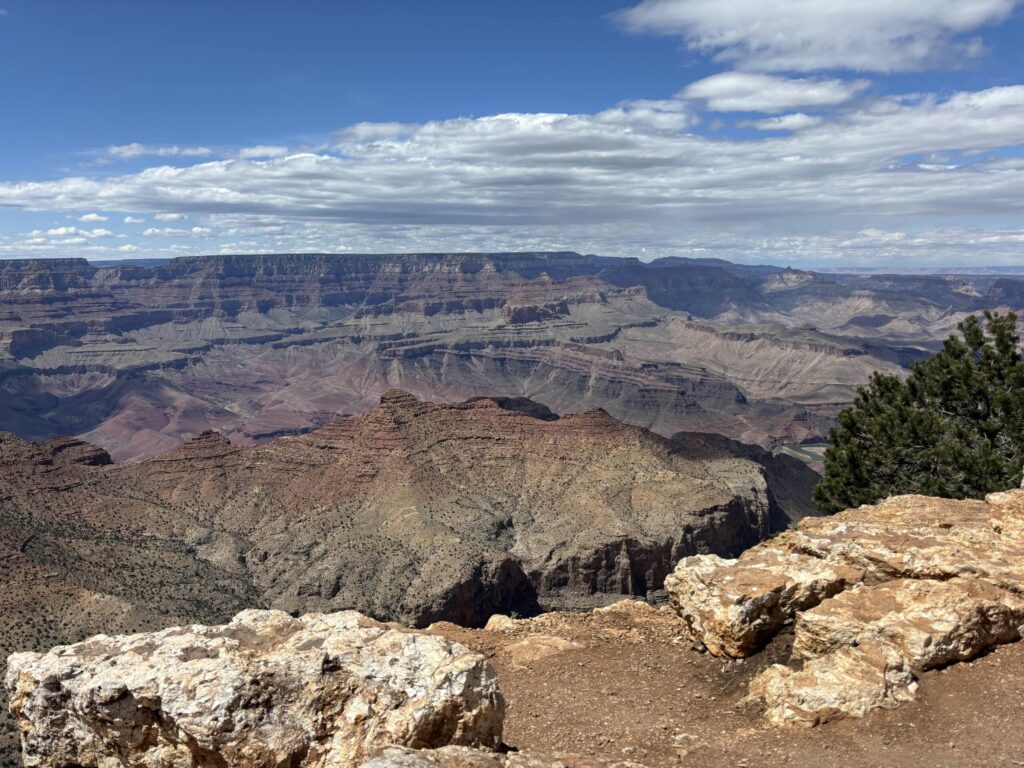 A photo looking into the Grand Canyon. There are blue skies with clouds, and the canyon stretches for miles in the distance.